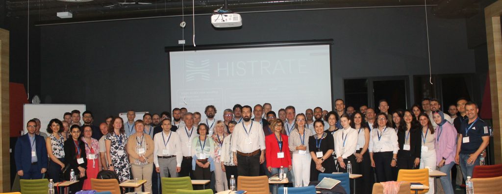 Group photo of the Histrate Conference participants in the venue in front of a large screen